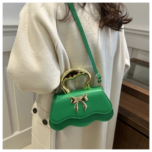 Detail of lime green crossbody bag with metallic bow and curved gold handle on white coat