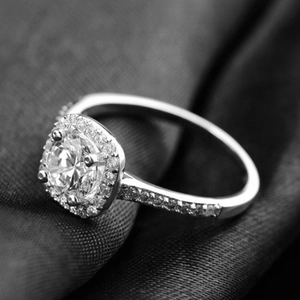 Macro shot of s925 silver ring with a round center stone and diamond halo on dark fabric