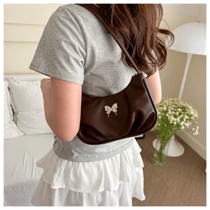 Detail of a dark brown pleated shoulder bag featuring a metallic butterfly clasp accent