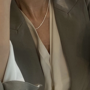Primo piano di una catena in argento scintillante minimalista indossata con un blazer elegante