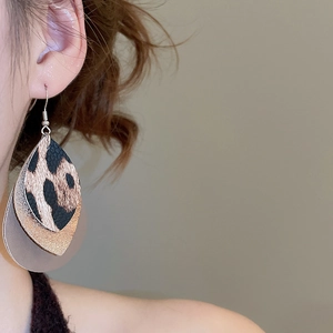 Macro detail of layered leopard print and gold glitter leaf earrings worn by model