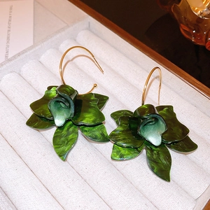 Macro view of dark green resin flower earrings with gold hooks on a white velvet tray