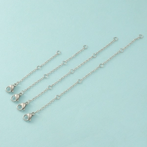 Detail of four silver stainless steel extender chains with lobster clasps on blue background