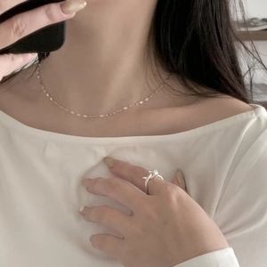Close-up of minimalist silver knot ring and fine gold chain necklace on a model