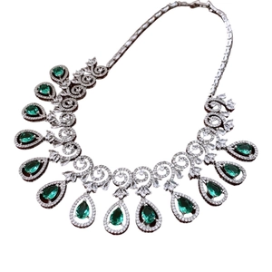 Silver necklace set with emerald teardrop stones and zircon crystals on white background