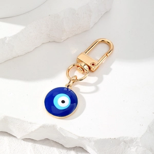 Golden Evil Eye keychain with blue enamel pendant on a minimalist stone background