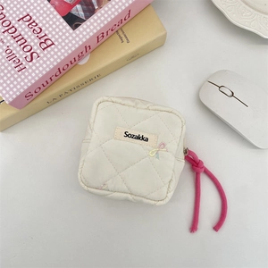 Detail view of a white quilted mini storage pouch with a pink cord zipper puller