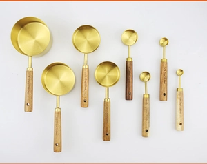 Detail of 8-piece gold stainless steel measuring set with acacia wood handles on white surface