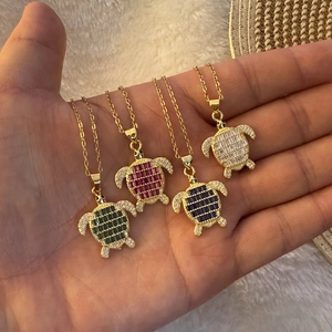Golden turtle pendant necklace set with colorful square zircons on a white plush background