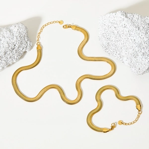 Elegant gold flat snake bone chain necklace and bracelet set on white stones