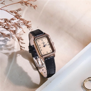 Detail view of rectangular rose gold watch with black leather strap on soft textured surface