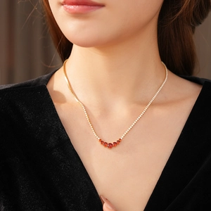 Close-up of elegant gold necklace with red zircons worn on model with black V-neck top