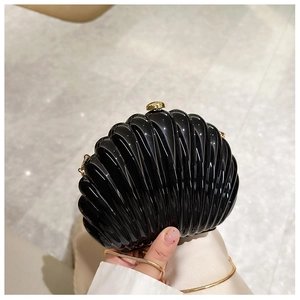 Macro detail of a black shell evening bag with glossy finish and gold metal chain strap