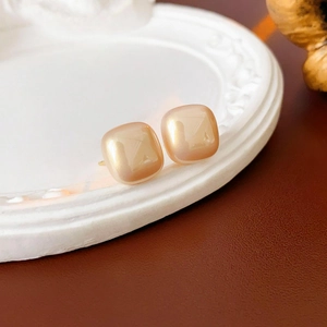 Detailed close-up of square champagne gold earrings with smooth pearl-like finish on tray