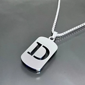 Macro d'un collier en acier titane argenté avec un pendentif plaque gravé d'une lettre D