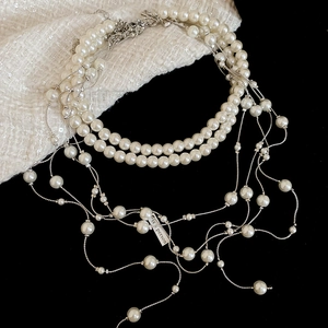 Detail view of multi-layer pearl fringe necklace on black background with tweed fabric
