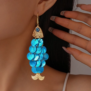 Detailed view of fish-shaped earrings with blue scales and evil eye charm on a model
