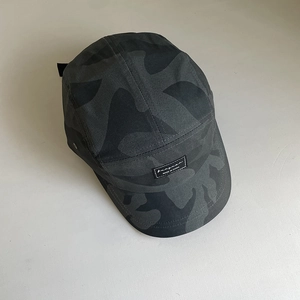 Detail view of a 5-panel camouflage camp hat featuring a black rectangular woven label tag