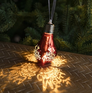 Glow red bulb ornament with Merry Christmas print hanging on a pine tree branch