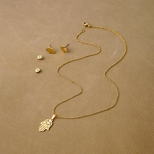 Detailed close-up of gold Hamsa Hand jewelry set with hollowed-out necklace and stud earrings