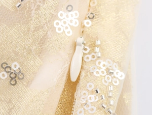 Close-up of beige mesh fabric with sequins, silver beads, and invisible zipper detail