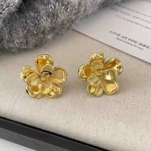 Polished golden 3D five-petal flower stud earrings on textured linen fabric