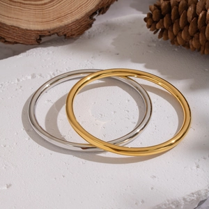 Minimalist circular stainless steel bangles in gold and silver finish on a wooden stand