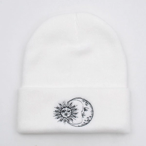 Close-up detail of sun and moon embroidery on a white knitted beanie hat fold