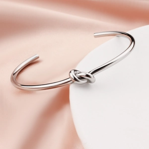 Minimalist silver stainless steel C-shaped cuff bracelet with a heart knot design on silk