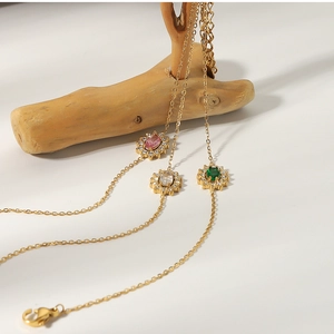Three gold-plated necklaces with pink, white, and green floral zircon pendants on a branch