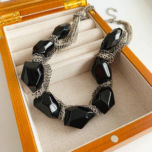 Detail of a black faceted gemstone necklace in a wooden jewelry box with velvet lining