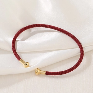 Macro shot of red braided rope bracelet with gold metal cylinder ends on silk background