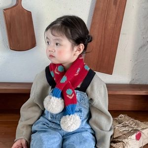Knitted red scarf with blue floral patterns and white pom-poms on a young girl