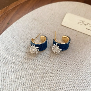 Detail view of denim-covered C-shaped earring with silver metallic snowflake accent