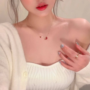 Close-up of gold-plated necklace featuring a red dog charm and a small red gemstone on model