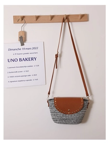 Detail of woven crossbody bag featuring brown PU leather flap and gold rivet accents