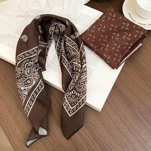 Detail of coffee brown paisley print silk scarf draped over vintage books and wood surface