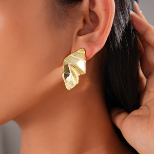 Detailed close-up of golden irregular geometric pleated earrings on a model's ear