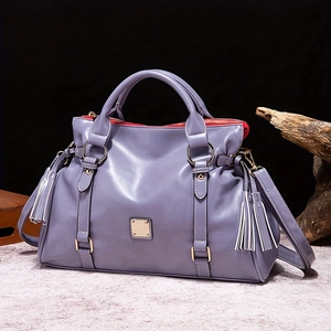 Detalle de bolso de cuero púrpura con borla decorativa y herrajes metálicos dorados