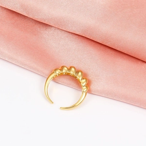 Macro view of a gold-finish textured croissant ring displayed on soft pink silk fabric