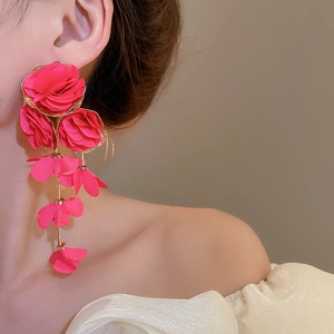 Detailed view of long rose-red chiffon fabric flower tassel earrings worn by a model