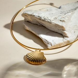 Artistic close-up of a gold shell pendant necklace displayed on white natural stones