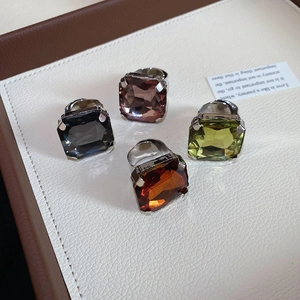 Detail of square-cut faceted crystal rings in four colors on a cream leather surface