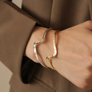 Close-up of gold and silver irregular wavy cuff bracelets on wrist with dark blazer