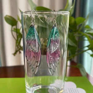 Detailed close-up of gradient green-pink cicada wing earrings on a glass rim