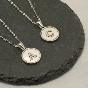 Detail of silver letter A and C pendants with white shells on black stone