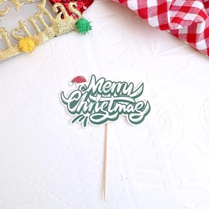 Macro detail of Merry Christmas cake topper with green font, white border and wood stick