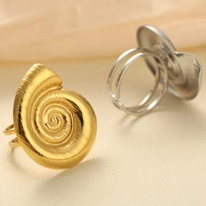 Detail of adjustable spiral shell rings in gold and silver finish on textured surface