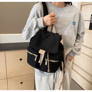 Detalle de mochila de lona negra con correas beige y cremalleras metálicas doradas