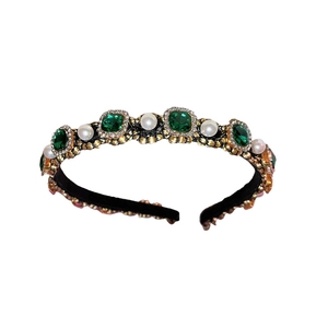 Vintage style black and gold headband with emerald green gems and white pearls on white background